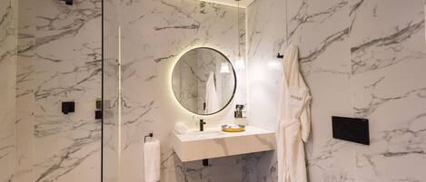 A modern bathroom with a marble wall, a round mirror, a white sink, and a towel rack.