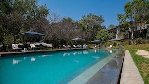 A swimming pool with lounge chairs and umbrellas, surrounded by trees and a building.