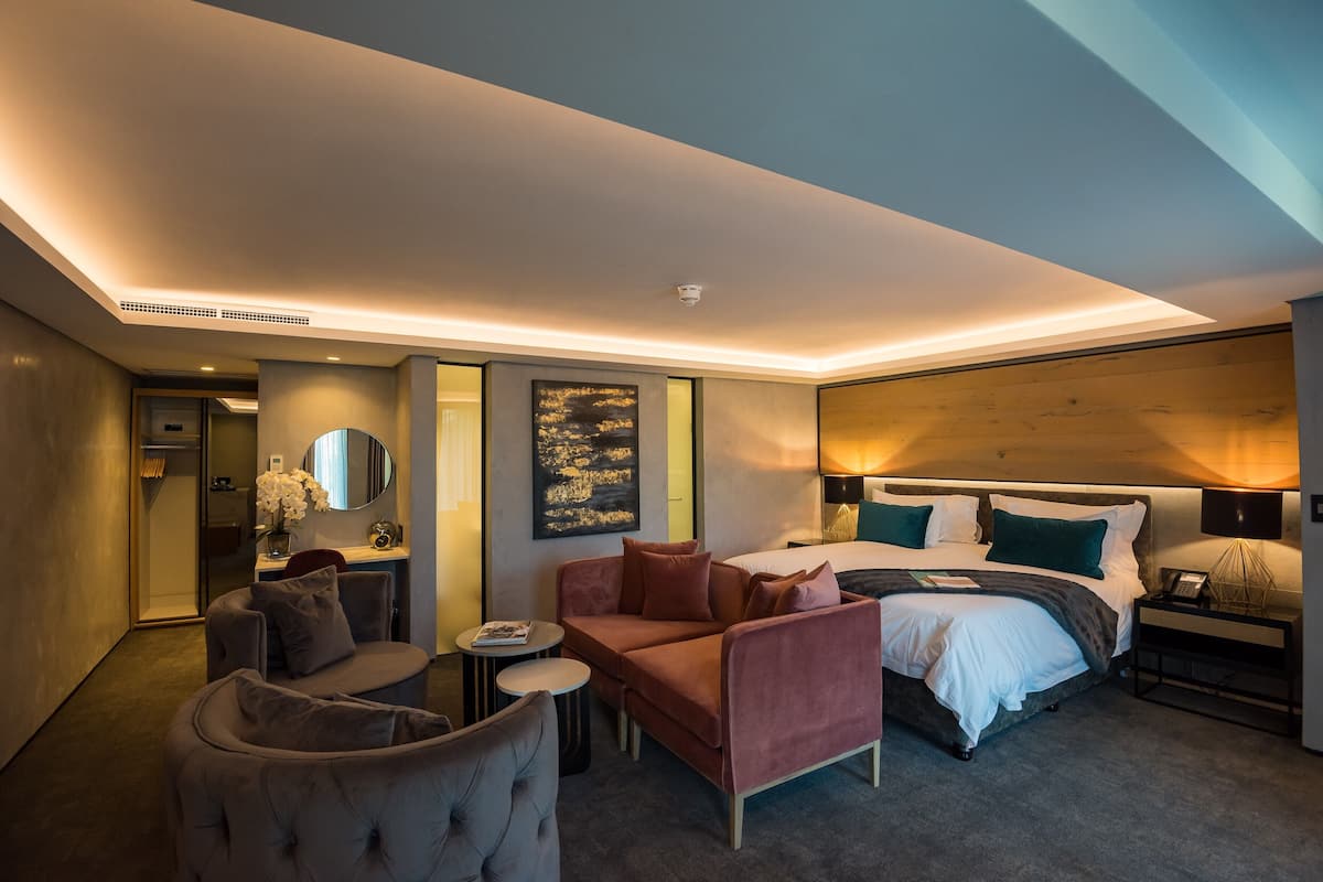 Ein modernes Hotelzimmer mit Bett, Sofa, Sessel, kleinem Tisch und Spiegel.