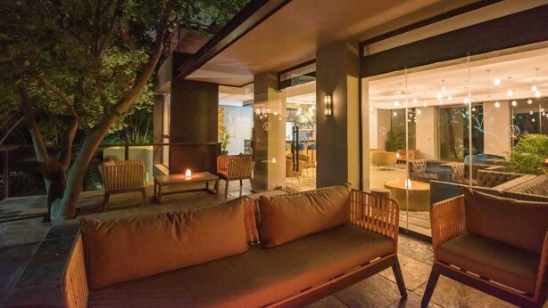 An outdoor seating area with a sofa and chairs, a fire pit, and a glass wall overlooking the interior.