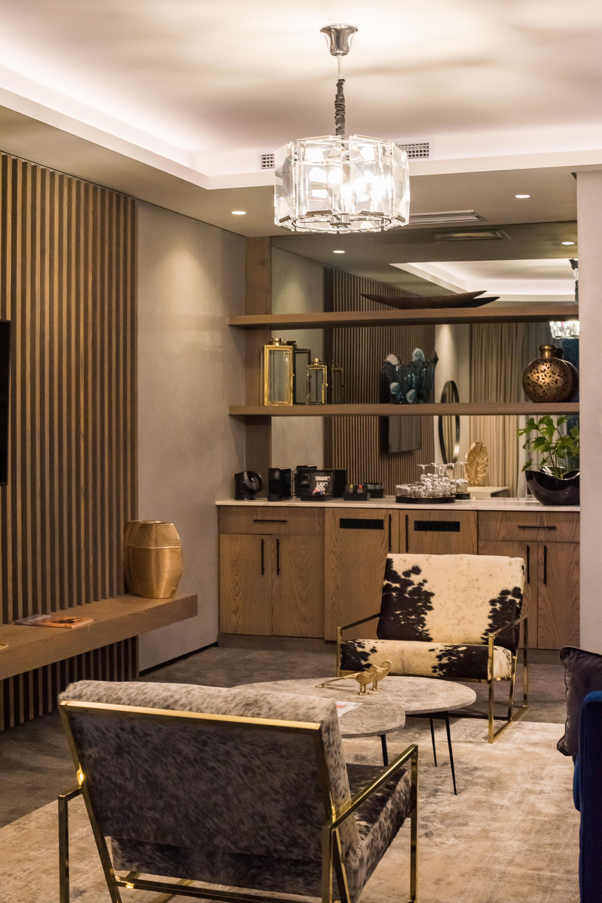 A modern interior with a round table, two chairs, a chandelier, wooden cabinets, and decorative items on shelves.