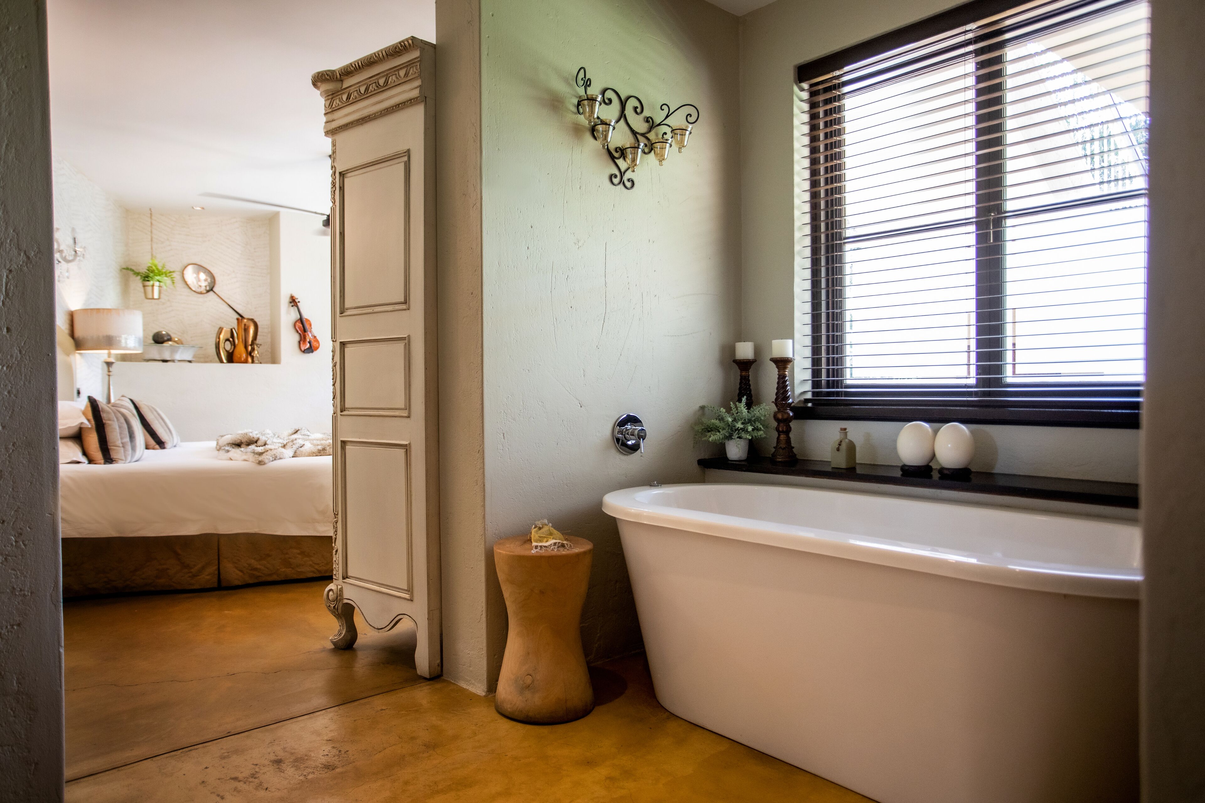 Un baño con una bañera independiente, un tocador con espejo y una ventana con persianas.