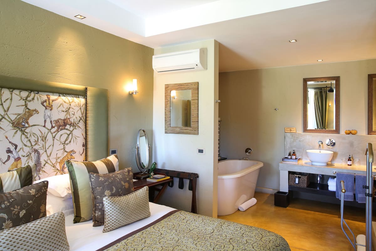 A bedroom with a large bed, a nightstand, a mirror, and a wall-mounted air conditioner.