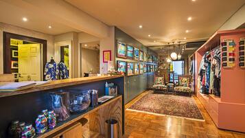 A hotel lobby with a reception desk, a display of colorful jars, a patterned rug, and a clothing rack.