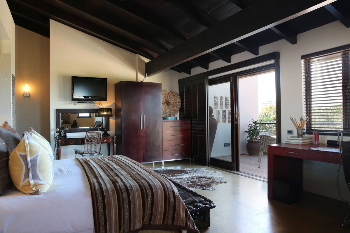 A hotel room with a bed, a desk, a TV, a wardrobe, and a sliding door to a balcony.