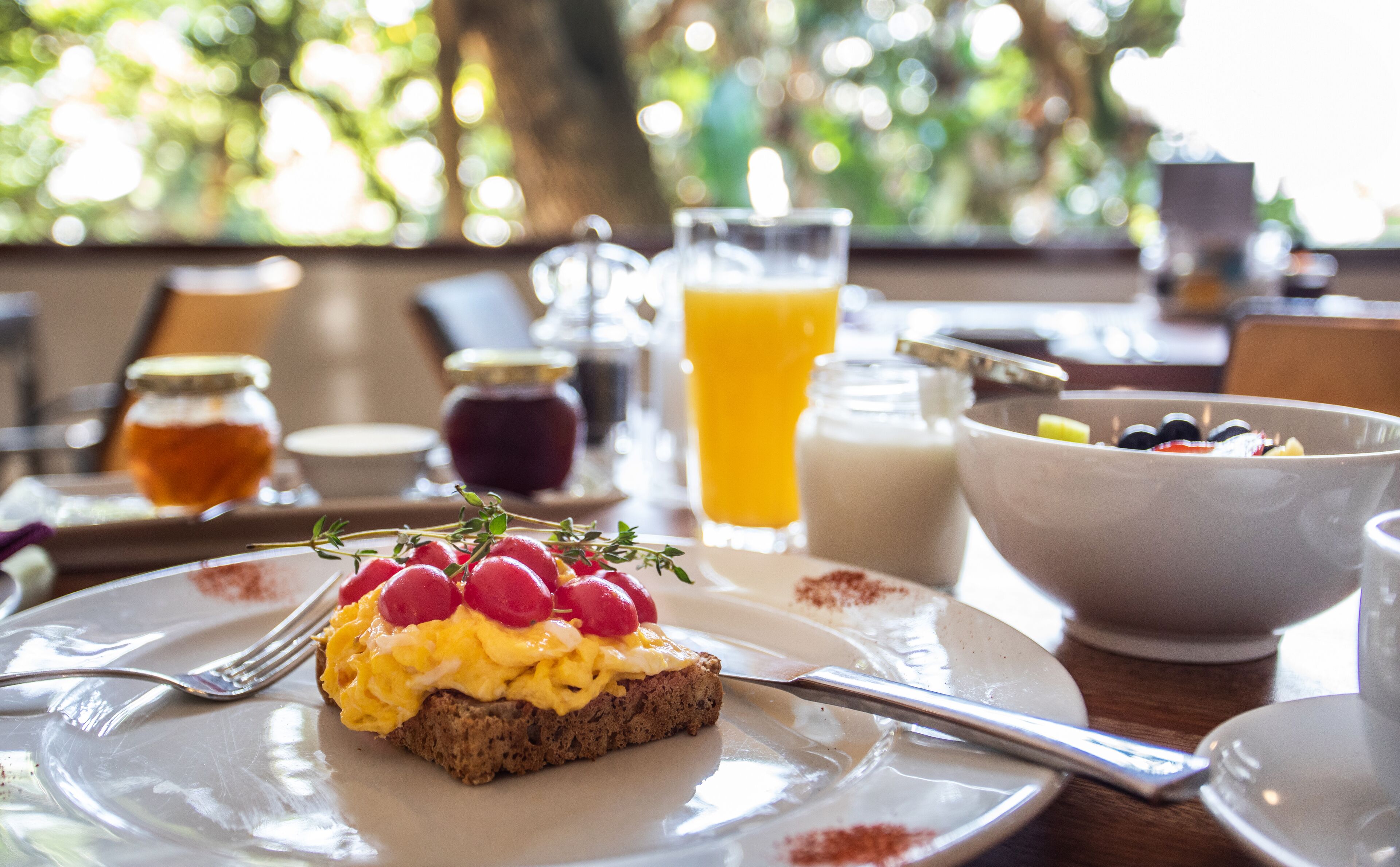 Une table mise pour le petit-déjeuner avec une tranche de pain grillé garnie d’œufs et de fruits rouges, un verre de jus d’orange et un bol de céréales.