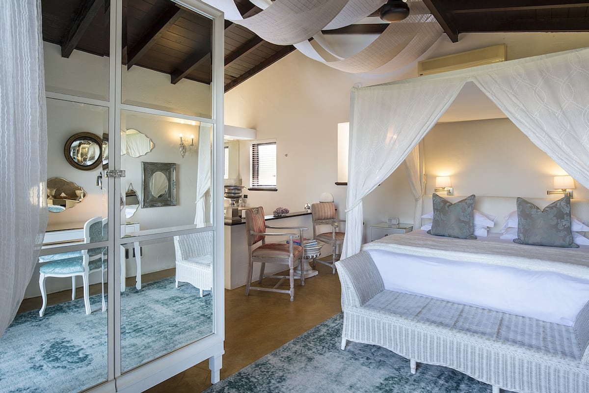 A bedroom with a canopy bed, a sitting area with chairs, a desk, and a mirror.