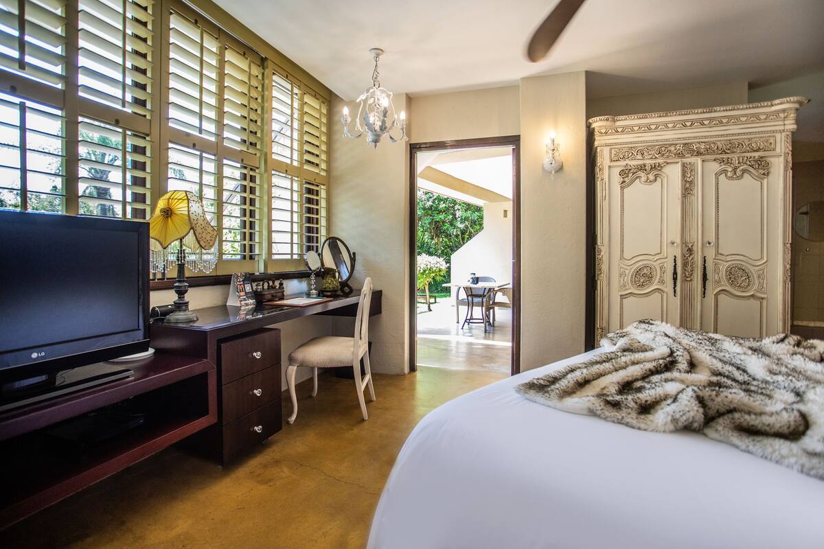 A hotel room with a bed, a desk with a TV, a chair, a wardrobe, and a view of the outdoors.