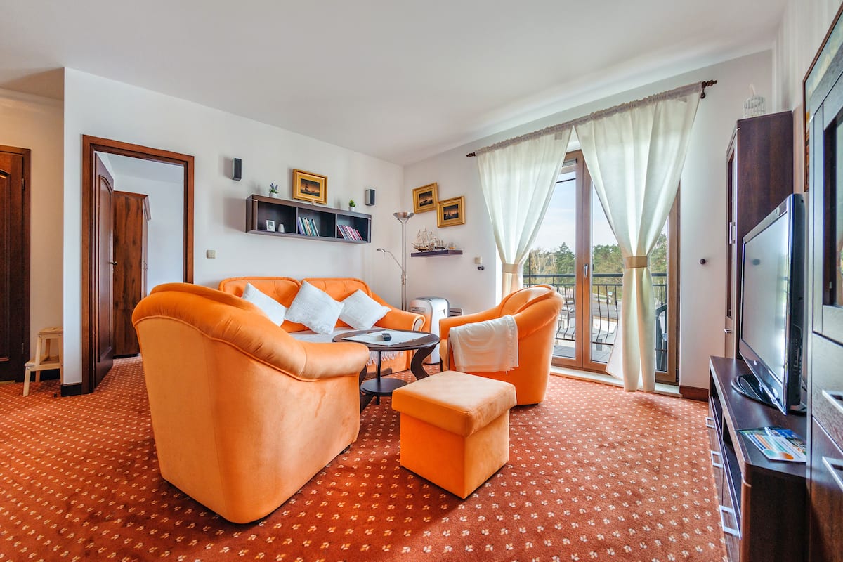 Una sala de estar con muebles naranja, televisor y un balcón con cortinas.