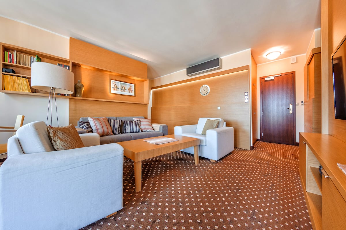 Una sala de estar moderna con un sofá, dos sillones, una mesita de centro, una estantería y un reloj en la pared.