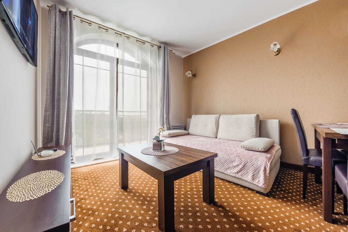 Una habitación de hotel con cama, una mesa, una silla, televisión y ventana con cortinas.