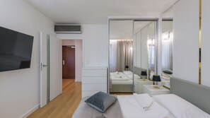 Una habitación de hotel moderna con una cama grande, un televisor de pantalla plana, un vestidor y un espejo que refleja la habitación.