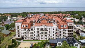 Un edificio grande de varios pisos con techo de tejas rojas, rodeado de vegetación y vistas al mar.