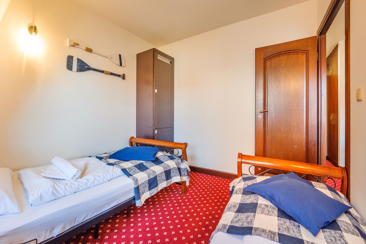Un dormitorio pequeño y bien iluminado con dos camas individuales, un armario y un espejo.