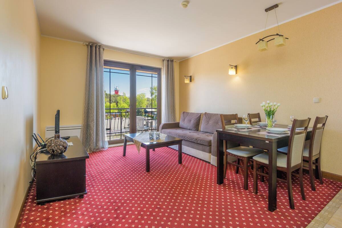 Una sala de estar con sofá, una mesa de comedor para cuatro personas y un balcón con vistas a zonas verdes.
