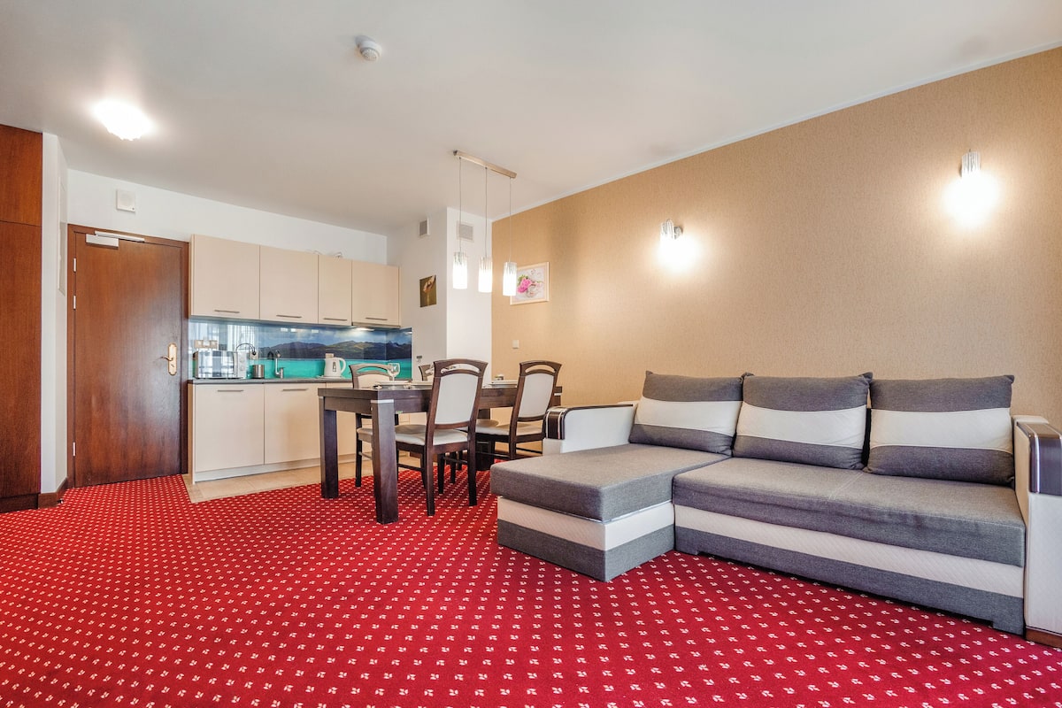Una sala de estar moderna con un sofá modular, una mesa de comedor con sillas y una zona de cocina.