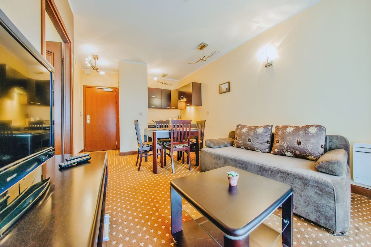 Una sala de estar con sofá, mesa de centro, televisor y un comedor con sillas y mesa.