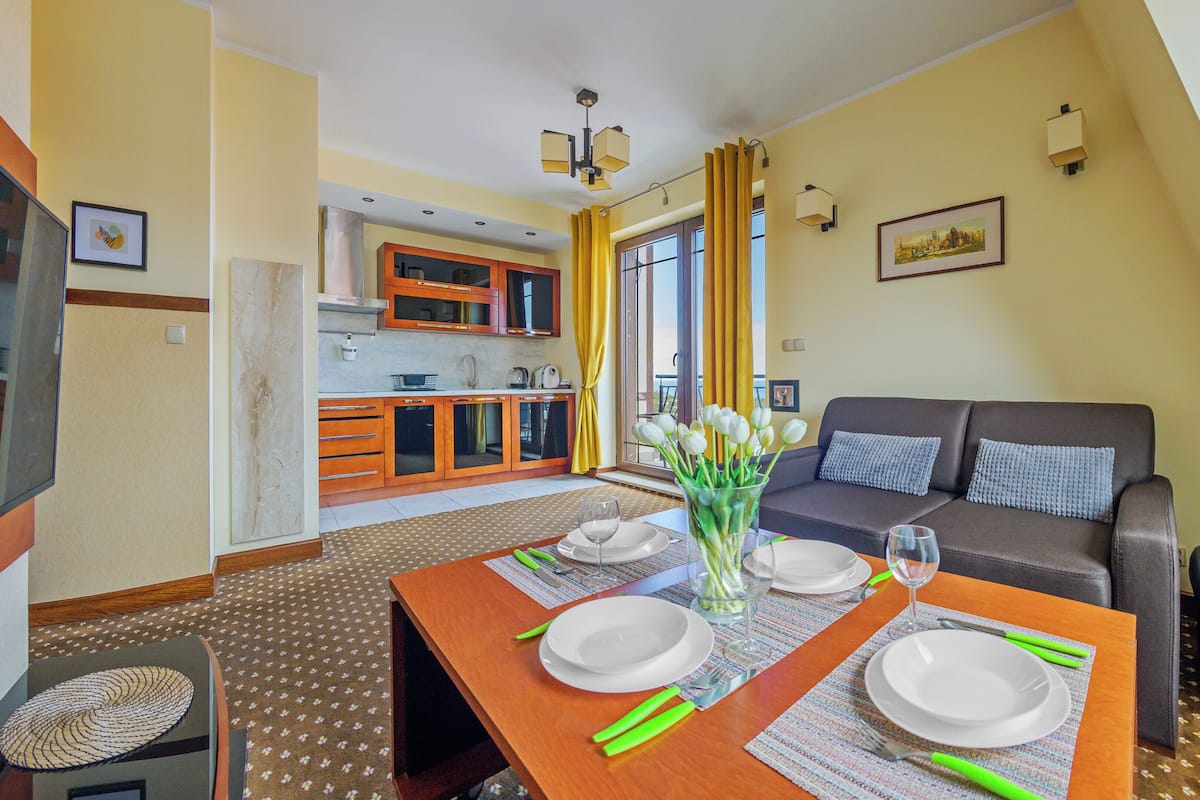 Un comedor con una mesa dispuesta para dos personas, un sofá y una cocina al fondo.