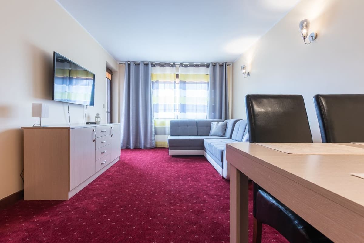 Una habitación de hotel con alfombra roja, un sofá, un televisor en la pared, una mesa de madera y un escritorio.