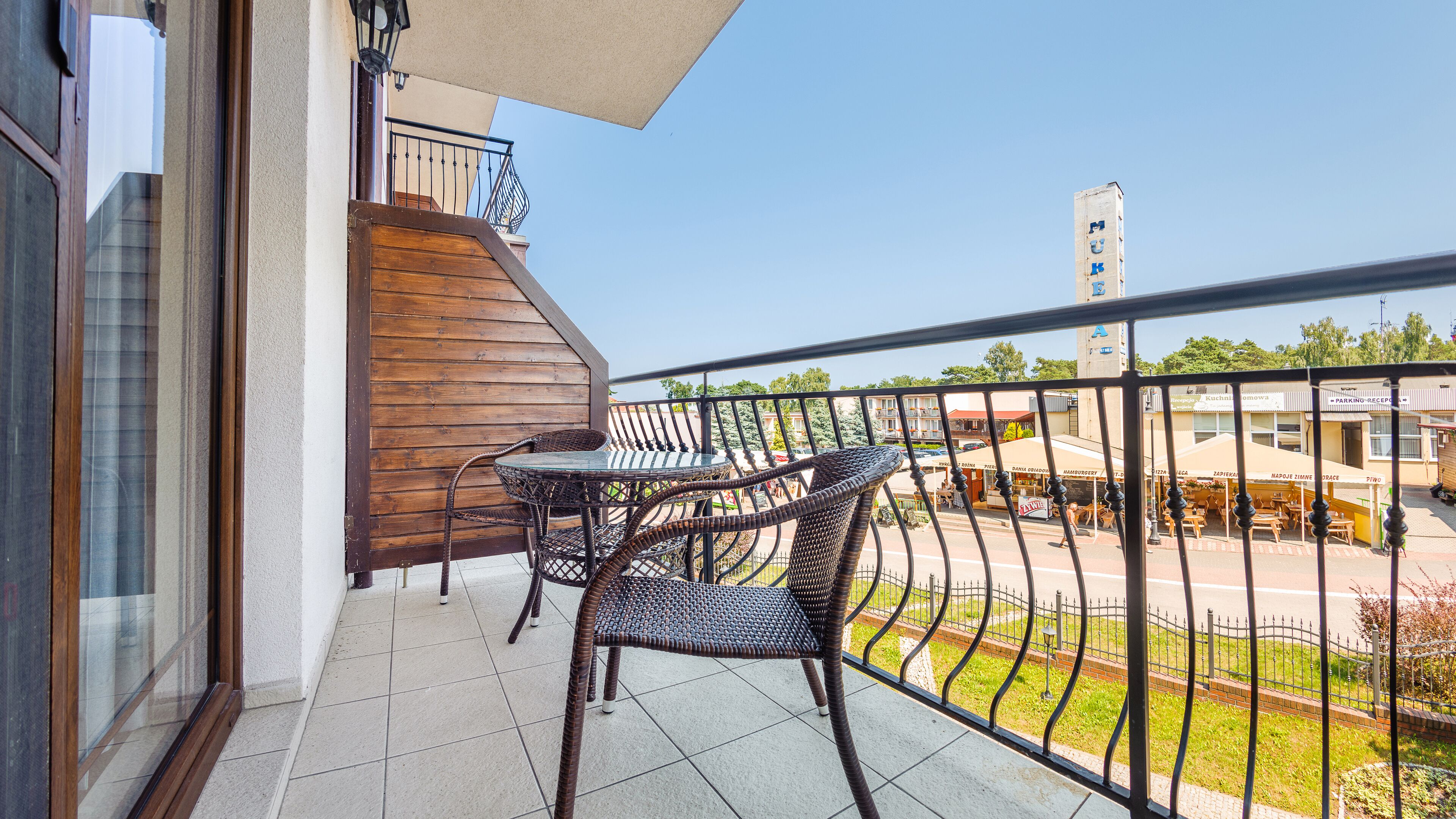 A balcony with a table and chairs, a view of the street, and a building in the background.