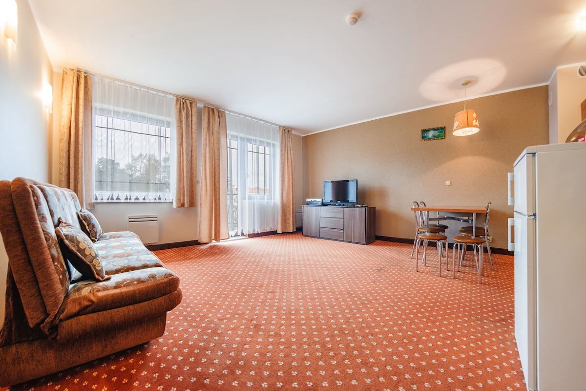 Habitación de hotel con sofá, una mesa de comedor con sillas, televisor y refrigerador.