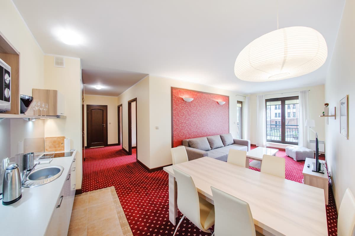 Una habitación de hotel moderna con zona de comedor, cocina y alfombra roja estampada.