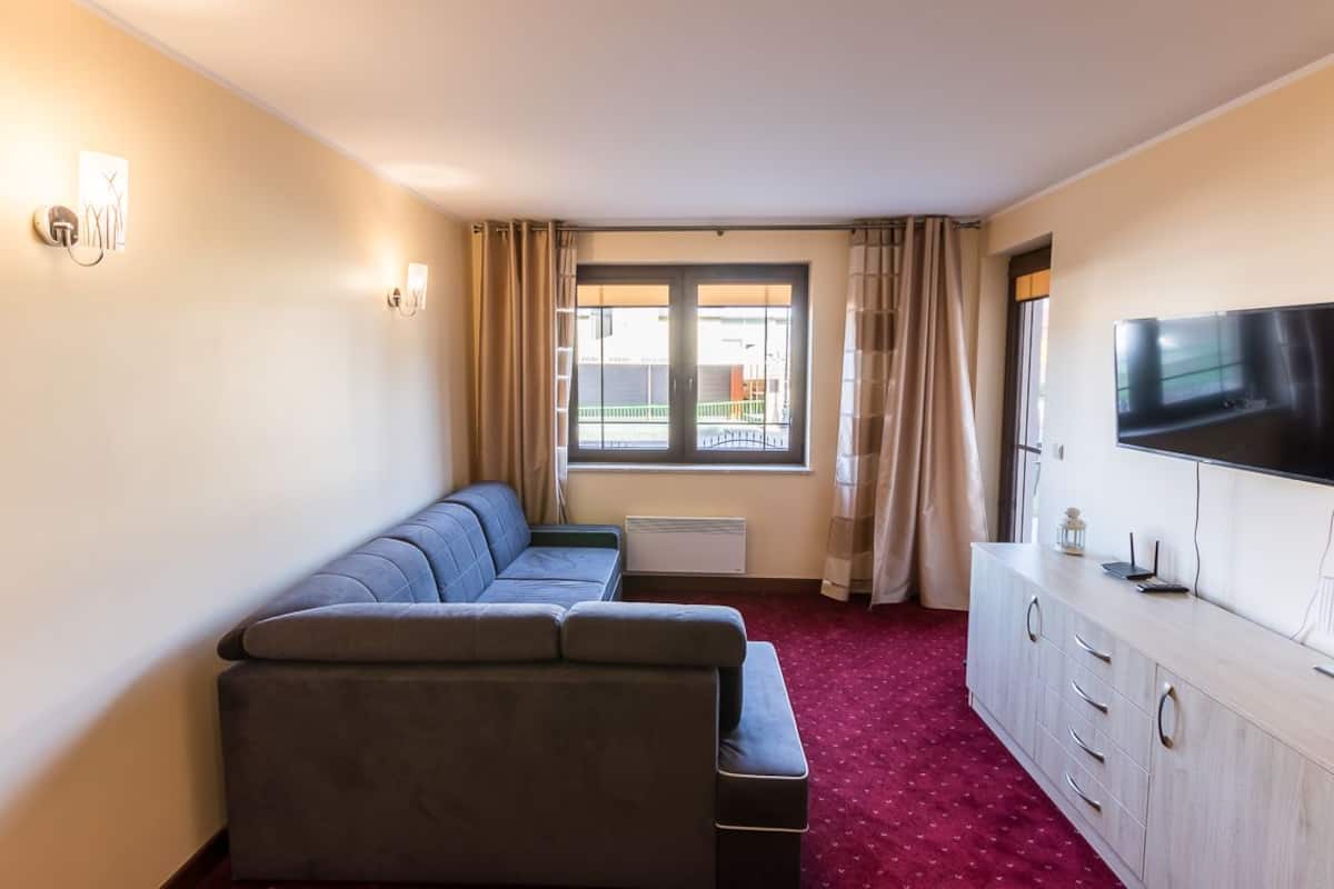 Habitación de hotel con sofá, televisor, armario y ventana con cortinas.