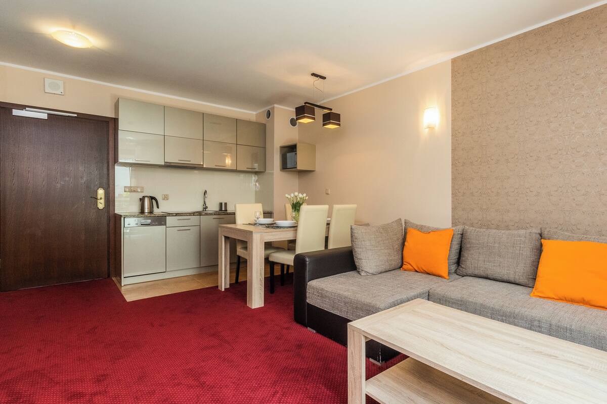 Un espacio habitable compacto con kitchenette, zona de comedor y sala de estar con sofá y mesa de centro.