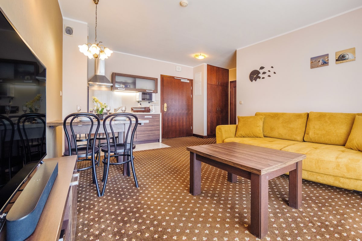 Una sala de estar con un sofá amarillo, una mesa de centro de madera y un comedor con sillas y una mesa.