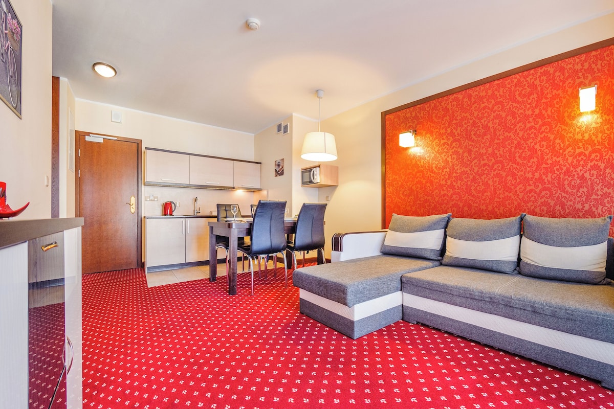 Una habitación de hotel compacta con kitchenette, zona de comedor y sofá cama.