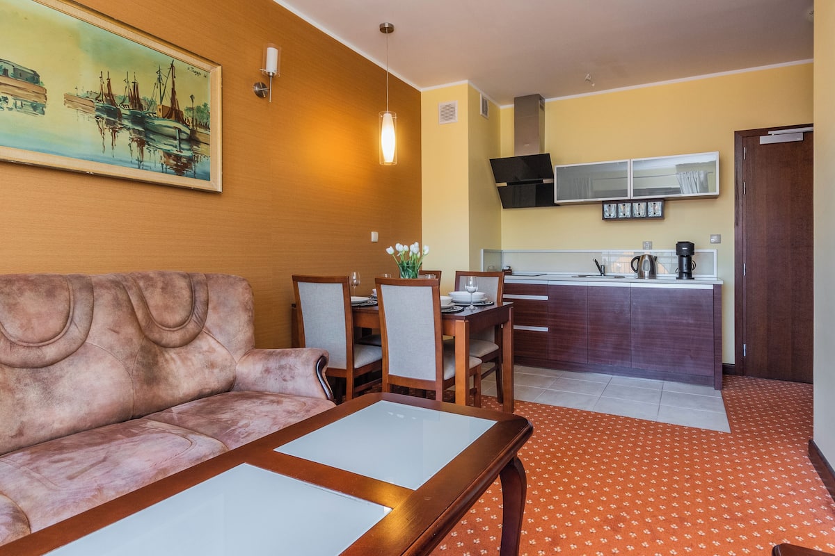 Una sala de estar con sofá, mesa de comedor, sillas y una cocina con estufa y alacenas.