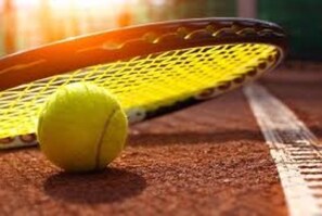 Een tennisracket en een bal op een gravelbaan.