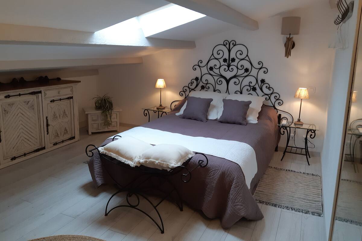 Quarto com cama, duas mesas de cabeceira, aparador, cabeceira decorativa, claraboia, armário e espelho.