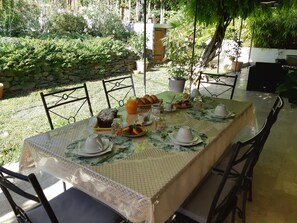 Una mesa al aire libre con mantel, platos, tazas y diversos alimentos.