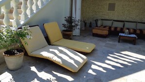 A sunlit outdoor seating area with a lounge chair and a sofa, a potted plant, and a staircase with white balustrades. - Les chambres Manon - Villa la Licorne (Belcodene)