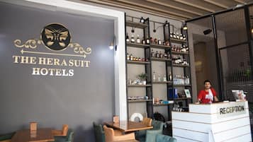 Ett entréområde med en receptionsdisk märkt med "RECEPTION", en vägg med hotellets namn "THE HERSUIT HOTELS" och en bardisk med hyllor fulla av spritflaskor.