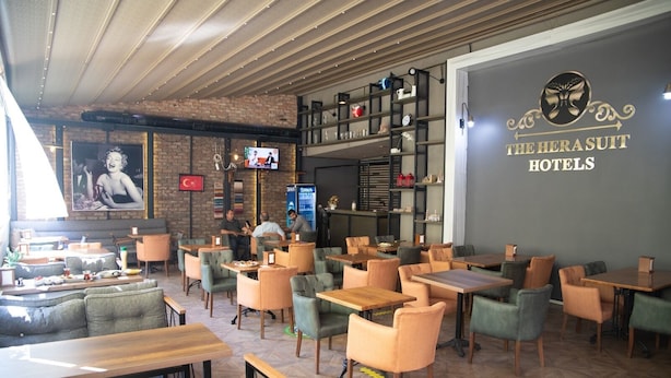A hotel restaurant with multiple seating areas, including tables and chairs, and a television screen in the background. - The Hera Suit Hotels (Istanbul)