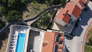 Vista aérea de una zona residencial con piscina, techos de tejas rojas y una entrada de vehículos curvada.