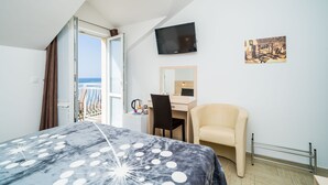 Un dormitorio con cama, escritorio, silla, televisor y un cuadro en la pared.