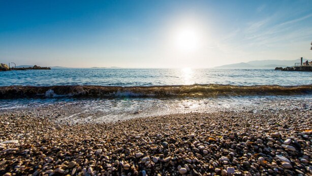 Una playa de piedras con el sol reflejado en el agua.