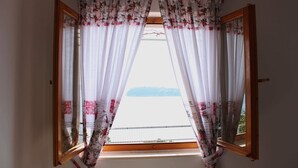 A window with open wooden shutters and sheer curtains with floral patterns.