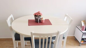 A round dining table with white chairs, a vase of pink flowers, and a small cupcake on a red placemat.