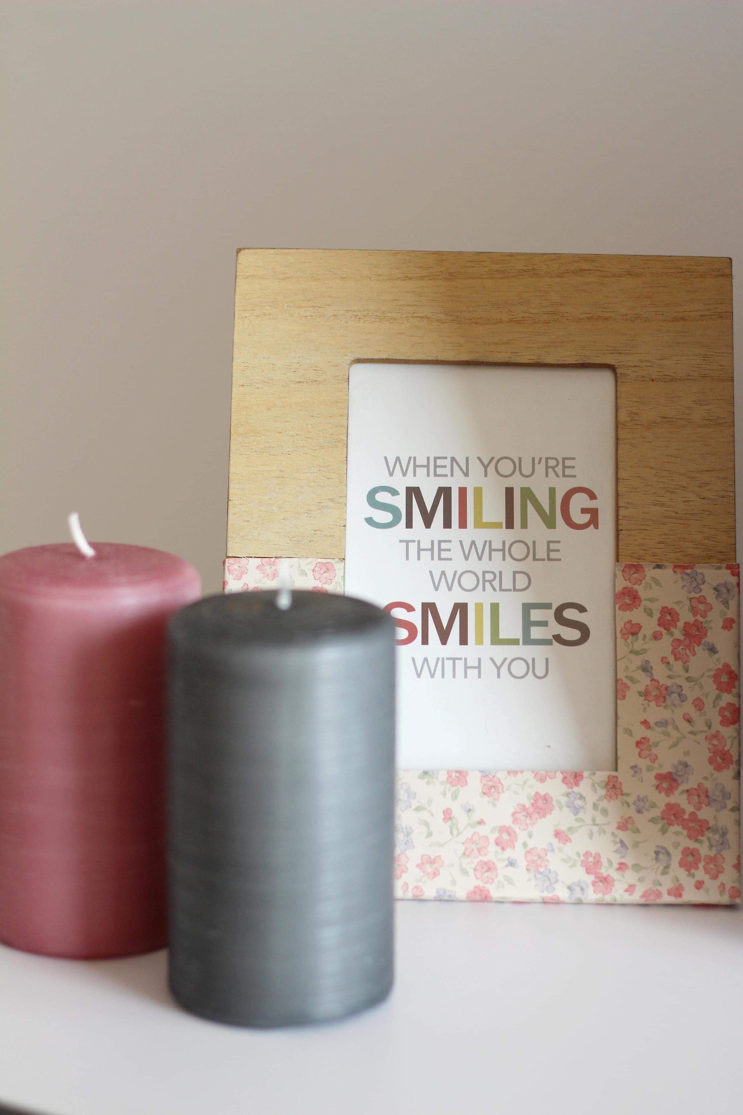 A wooden frame with a motivational quote and two candles, one red and one gray, on a white surface.