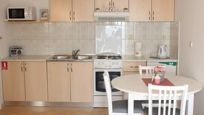 A compact kitchen with wooden cabinets, a microwave, a stove, and a sink.