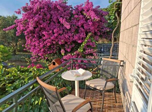 Een terras met twee stoelen en een tafel, omgeven door een tuin met een grote bloeiende boom.