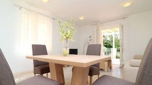 Un comedor con mesa de madera y cuatro sillas grises, un florero con flores y vista a la vegetación exterior.