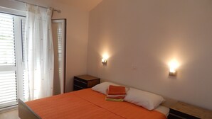 A bedroom with a bed, two bedside tables, a nightstand, and a sliding glass door. - Apartments Mimose - Two Bedroom Apartment with Terrace and Sea View (Milna)