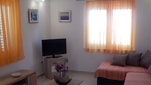 A living room with a flat-screen TV on a wooden stand, a sofa, a coffee table with a vase, and two windows with curtains. - Apartments Mimose - Two Bedroom Apartment with Terrace and Sea View (Milna)