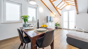 Un comedor con una mesa de madera, sillas y un bol de limones. Se ve un sofá y un televisor al fondo.