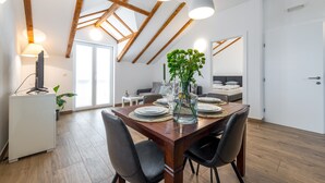 Un comedor con una mesa de madera preparada para cuatro personas, rodeada de sillas negras. Un ventanal grande permite que la luz natural ilumine el espacio, y hay una planta sobre la mesa.